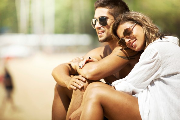 Romantic young couple sitting on the beach enjoying warm sun.